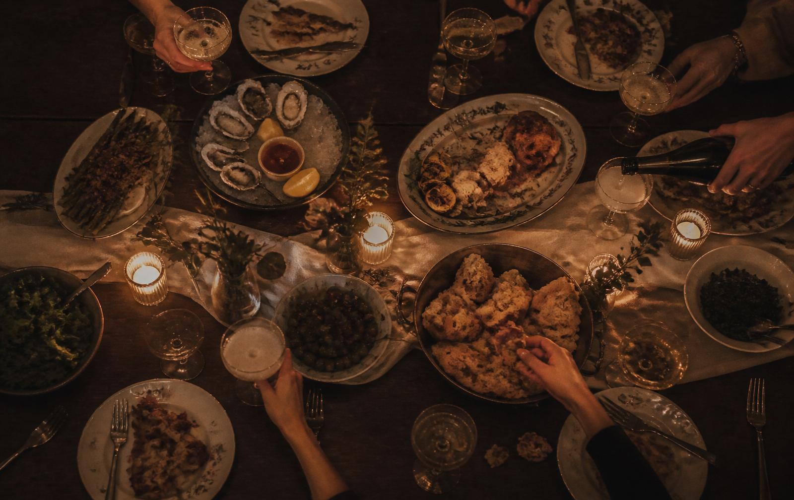 Overhead view of a candlelit dinner table with coupes of champagne, oysters and shared plates.